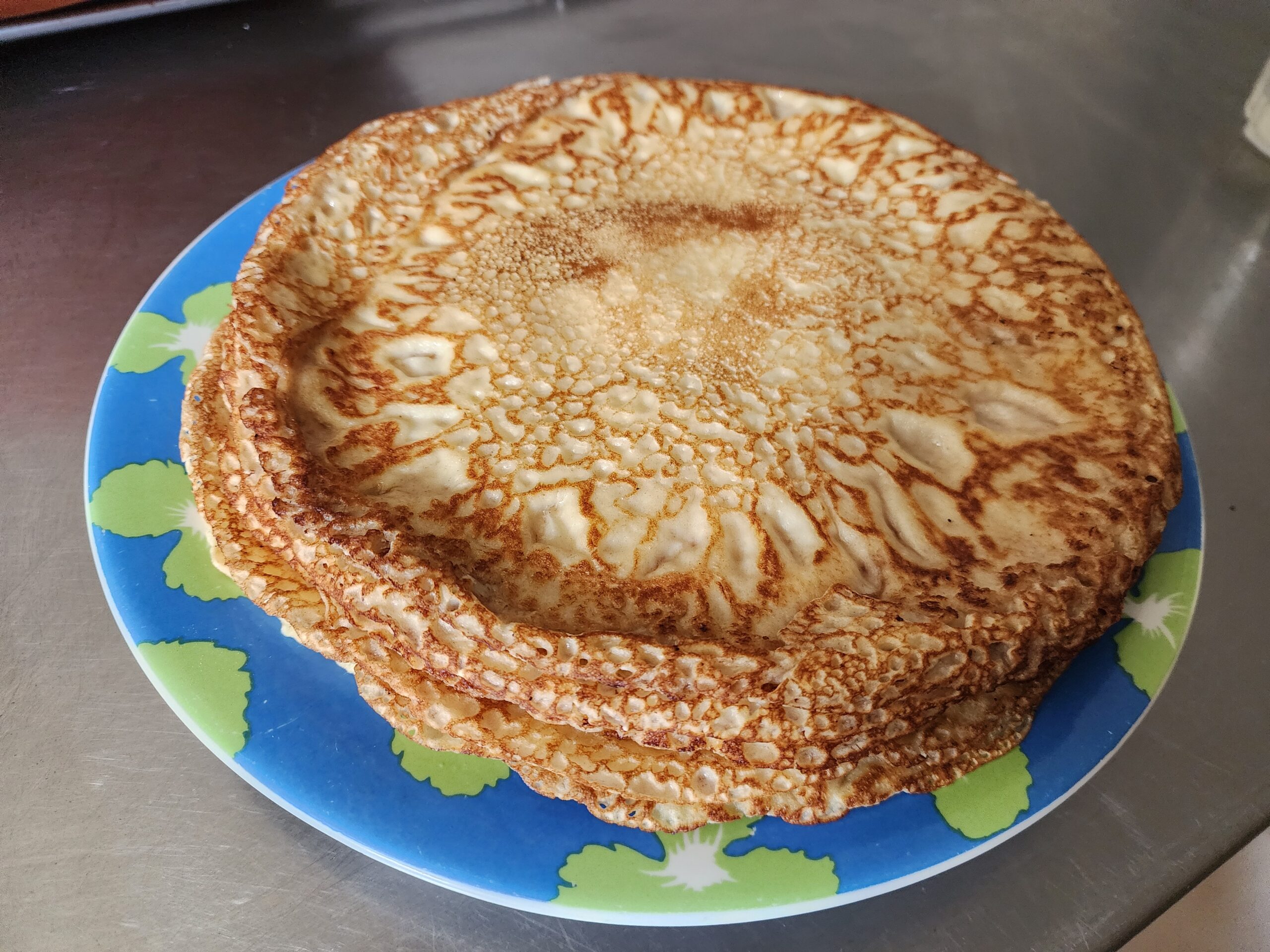 Stack of thin golden crepes on a blue and green plate