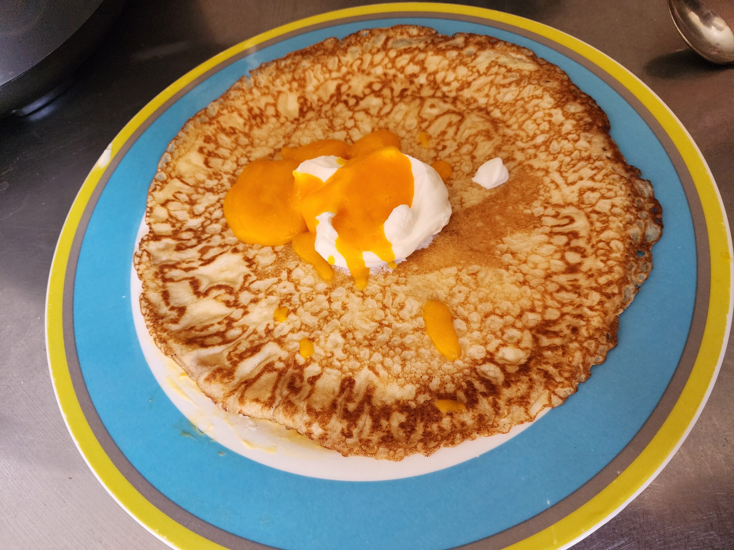 A single crepe on a plate topped with thick yogurt and mango puree