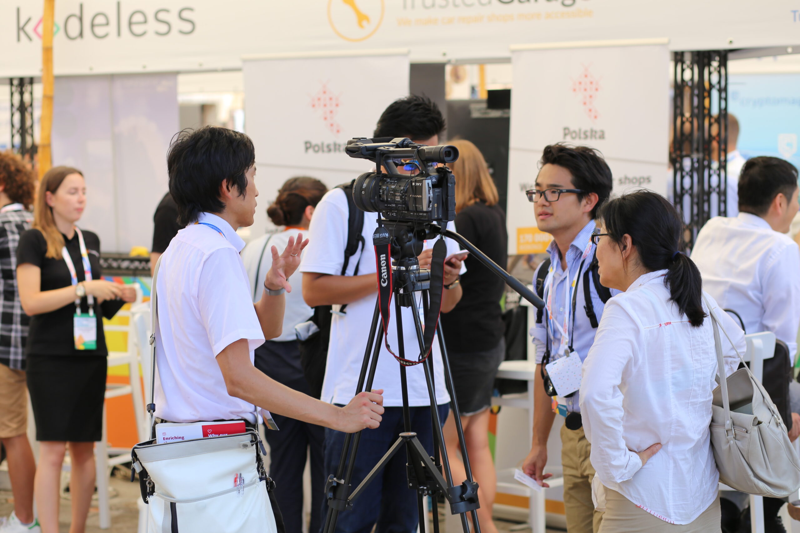 A camera operator crouches behind a broadcast camcorder on a tripod