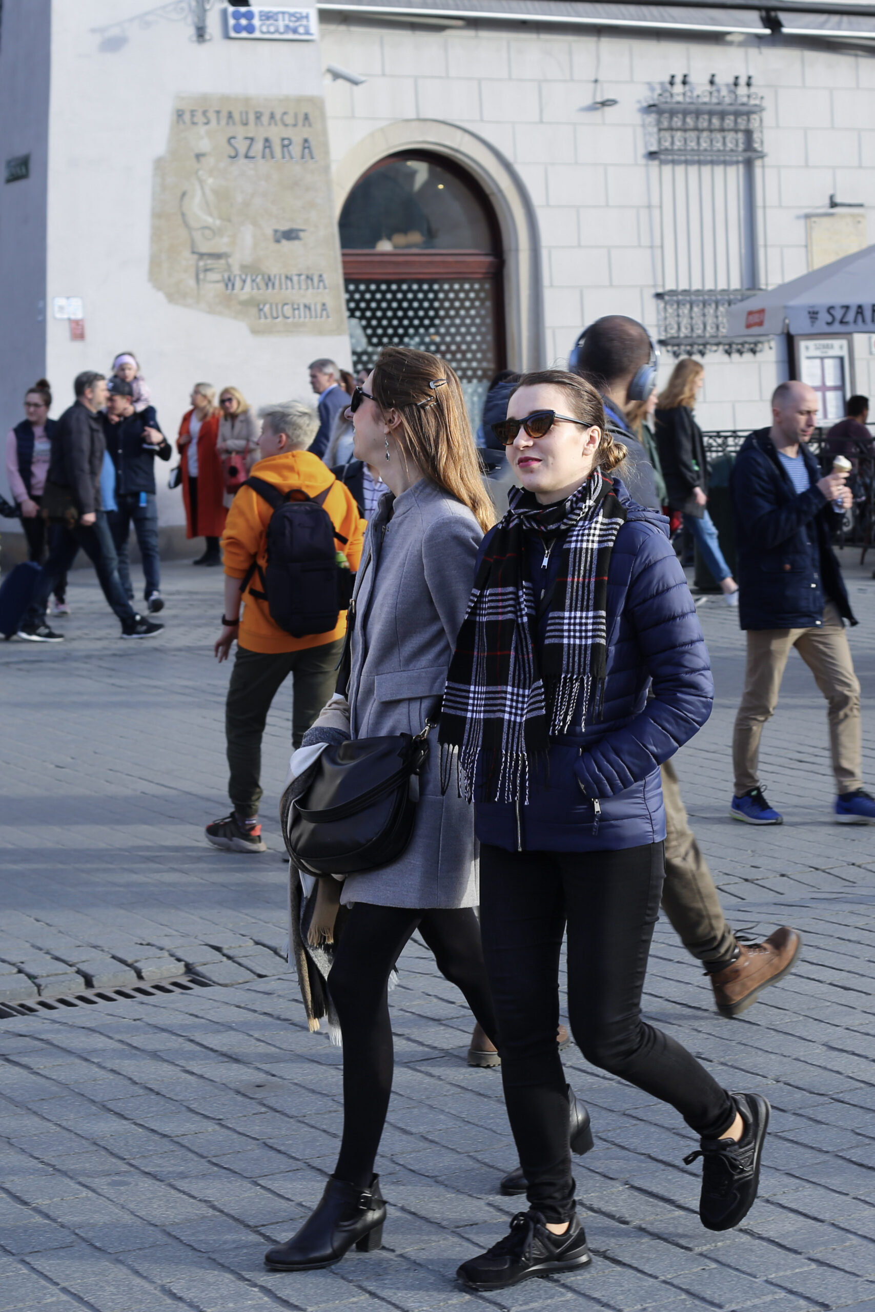 Two Women Walking Through Kraków's Main Market Square in Autumn Layers