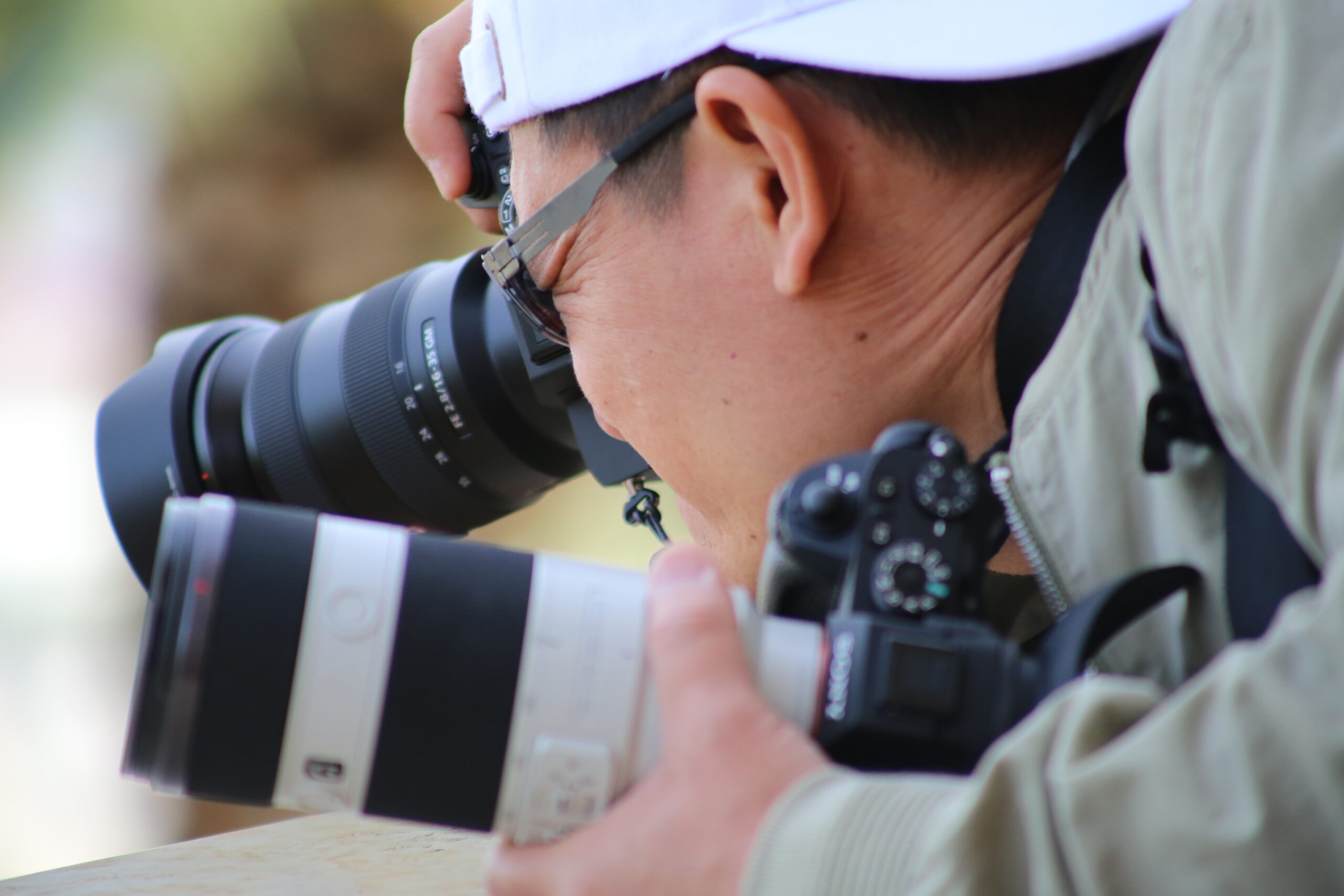 Photographer in a white cap using a Tamron 150-500mm zoom while holding a second Sony camera with a white Sony telephoto lens