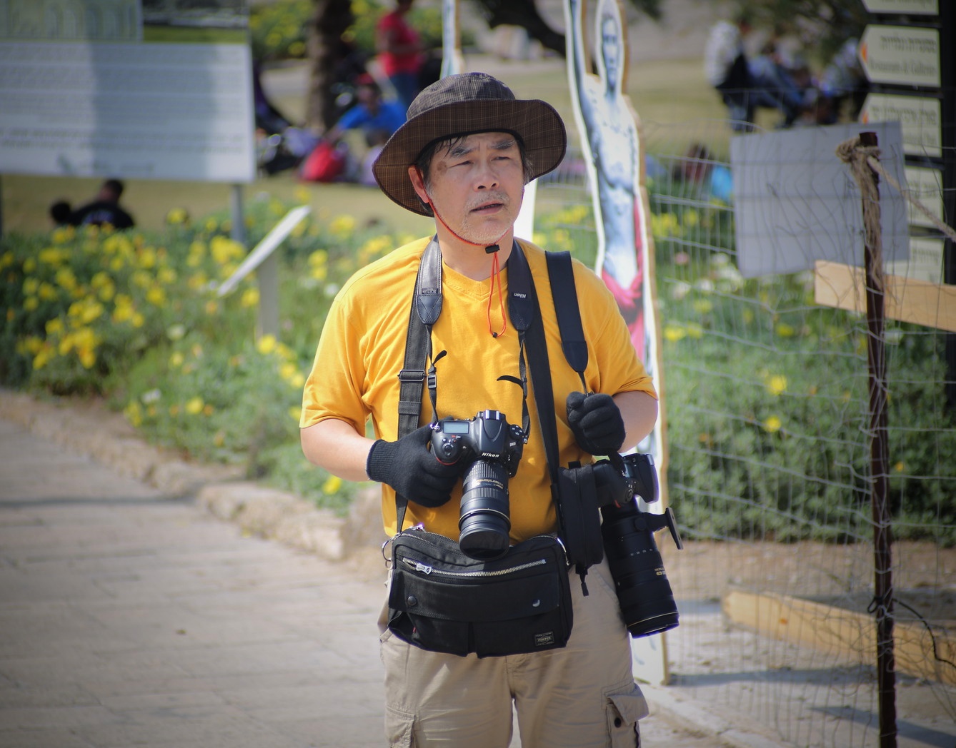 Outdoor photographer carrying two Nikon DSLR cameras, one with a standard zoom and the other with a long telephoto lens