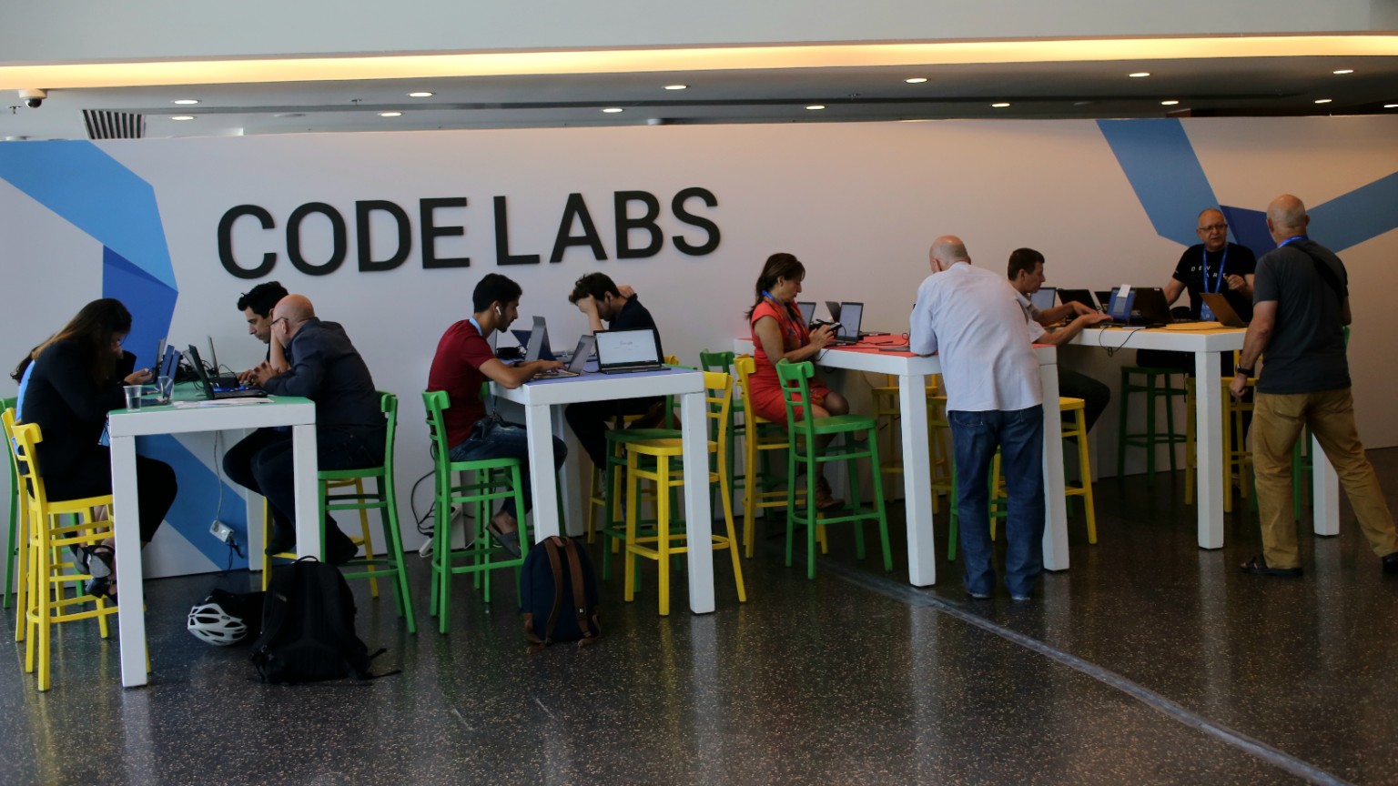 People working together and individually on laptops around tall white tables, with green and yellow chairs beneath a large CODE LABS sign.