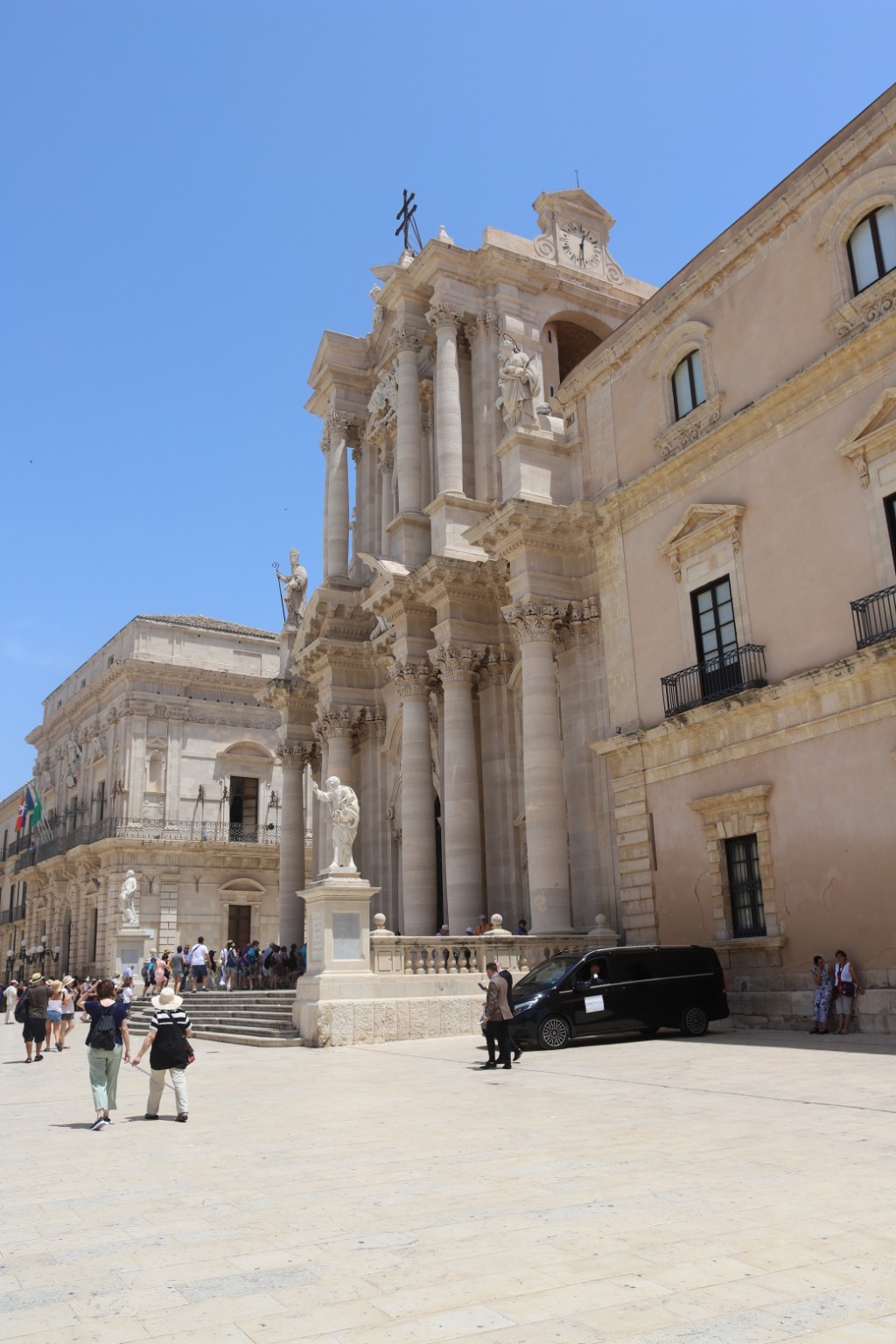 The sunlit Baroque facade of Syracuse Cathedral in Ortigia, with visitors crossing Piazza Duomo